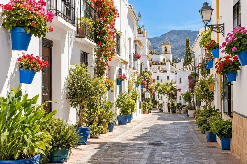 Calle del casco antiguo de Estepona con casas blancas y macetas de flores de colores en una tarde soleada andaluza