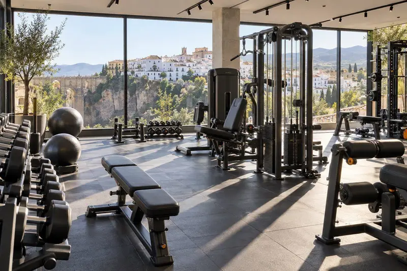 Interior de un gimnasio en Ronda con máquinas de musculación y vistas al pueblo blanco andaluz a través de grandes ventanales